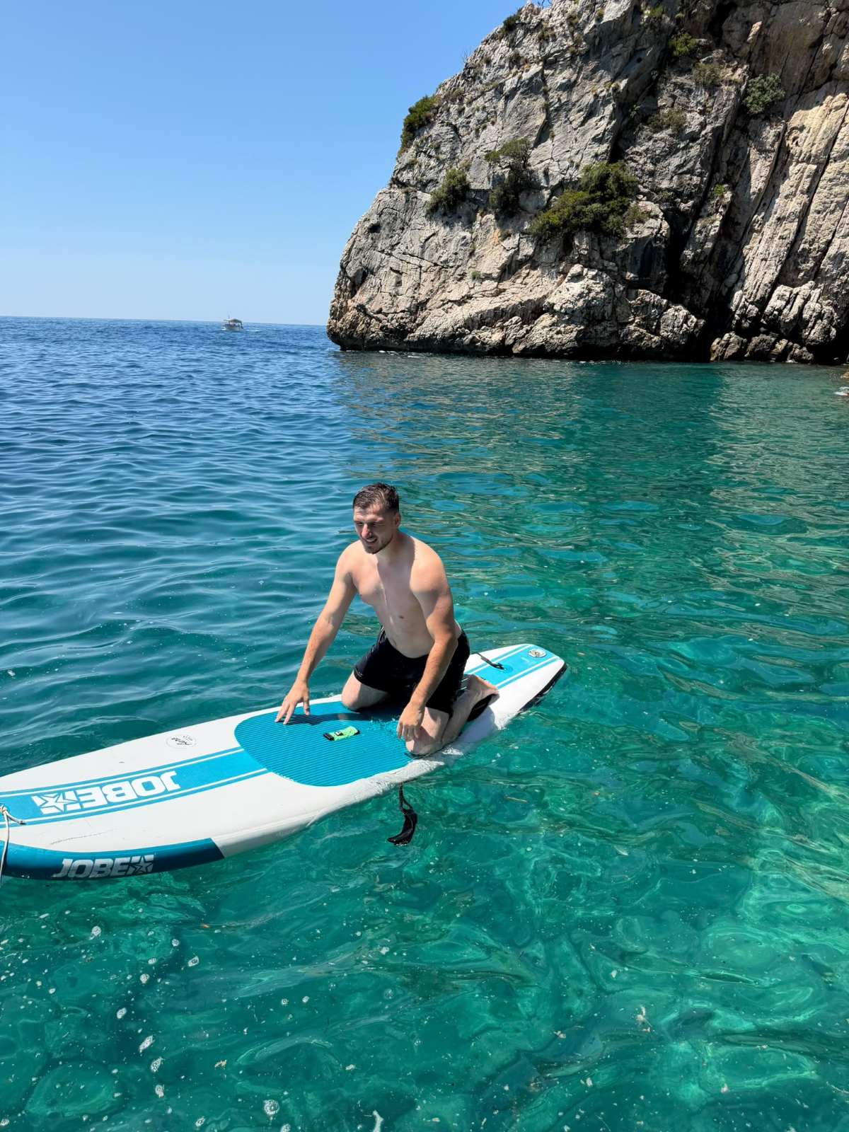 Paddleboarder in turquoise water beside the cliffs